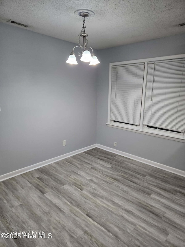 unfurnished room with a textured ceiling, visible vents, baseboards, wood finished floors, and an inviting chandelier