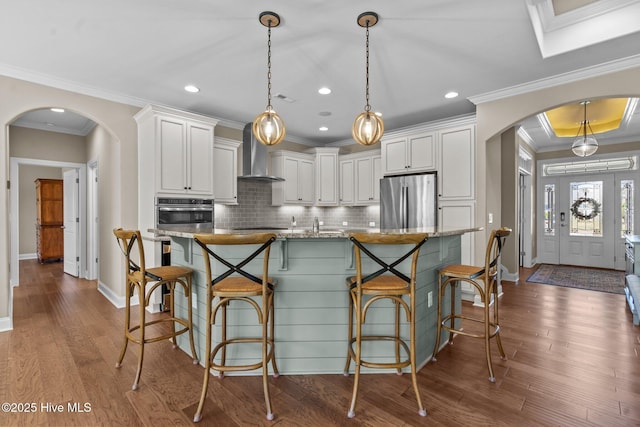 8549 Oak Abbey Trl NE, Leland, NC 28451 - kitchen featuring stainless steel appliances, arched walkways, wall chimney exhaust hood, crown molding, and tasteful backsplash