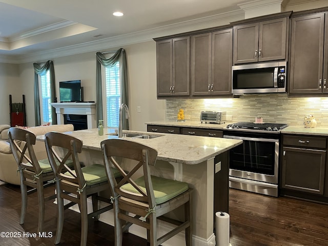 kitchen with backsplash, a sink, open floor plan, ornamental molding, and stainless steel appliances