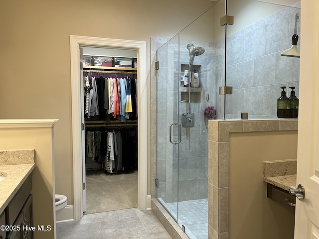 bathroom with a walk in closet, tile patterned flooring, a shower stall, vanity, and toilet