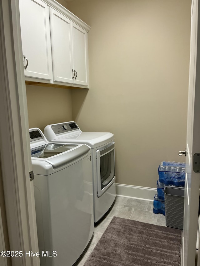 clothes washing area with washing machine and clothes dryer, baseboards, and cabinet space