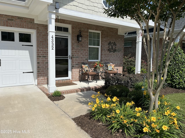 entrance to property with a porch, brick siding, driveway, and a garage