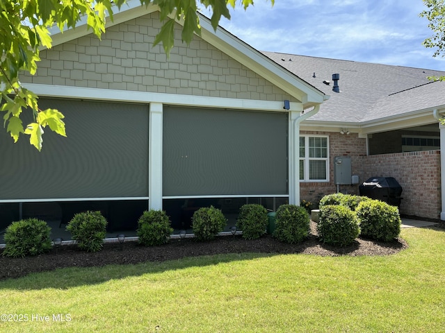 view of side of property featuring brick siding, a shingled roof, a yard, and a sunroom