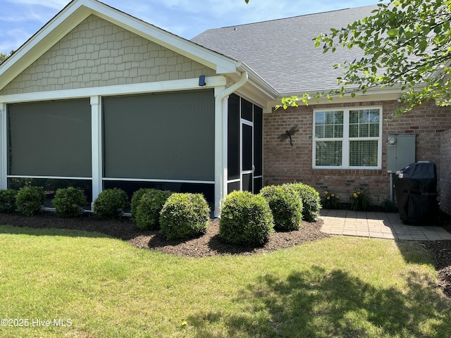 view of side of property featuring a lawn, brick siding, a shingled roof, and a sunroom