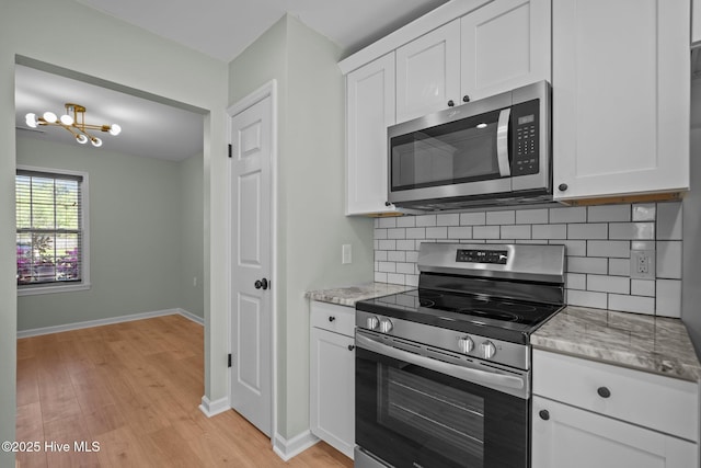 kitchen featuring light wood-style flooring, tasteful backsplash, white cabinetry, appliances with stainless steel finishes, and a notable chandelier