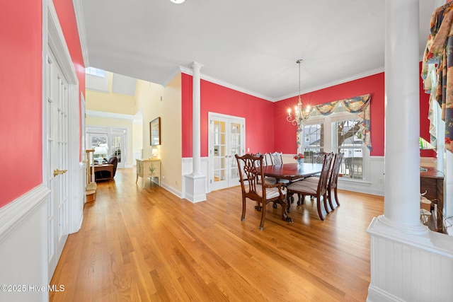 dining space featuring light wood finished floors, french doors, decorative columns, and wainscoting