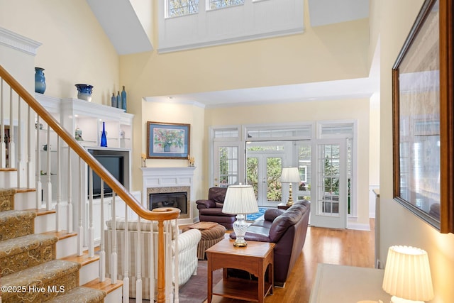 living area featuring wood finished floors, a towering ceiling, french doors, stairs, and a glass covered fireplace
