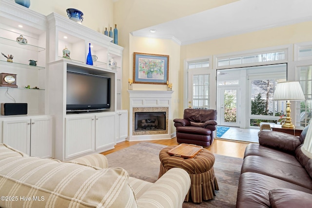 living area featuring a fireplace, built in shelves, light wood-style floors, and crown molding