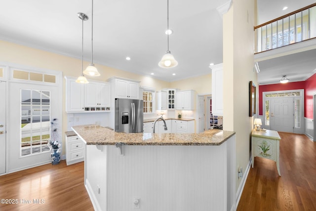 kitchen with light stone countertops, ornamental molding, wood finished floors, a sink, and stainless steel fridge