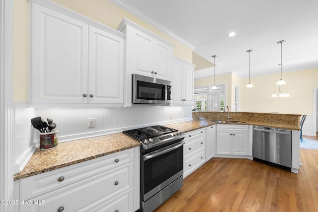 kitchen with a peninsula, white cabinetry, appliances with stainless steel finishes, light wood finished floors, and a sink