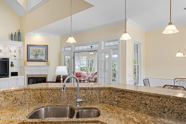 kitchen with a sink, hanging light fixtures, light stone counters, and crown molding
