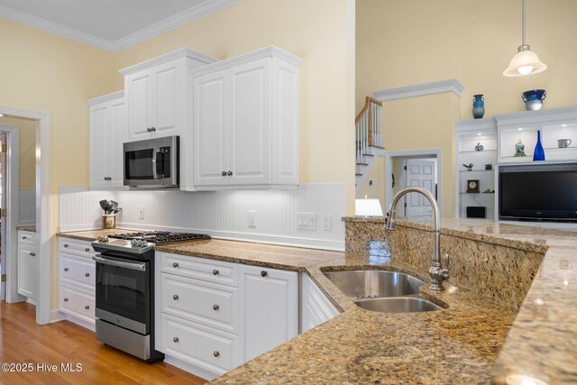 kitchen featuring white cabinets, a sink, crown molding, light wood finished floors, and stainless steel appliances