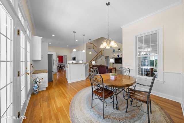 dining space with crown molding, light wood-style flooring, stairway, wainscoting, and a notable chandelier