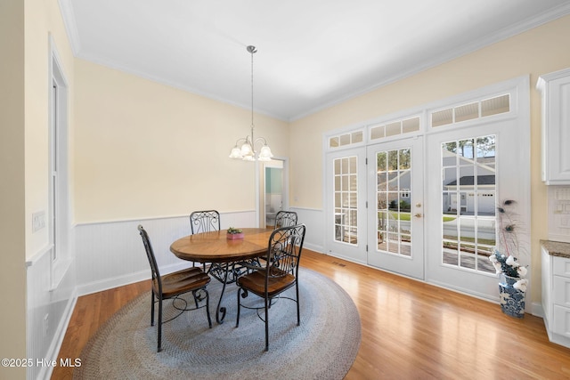 dining room featuring an inviting chandelier, ornamental molding, french doors, light wood-style floors, and wainscoting