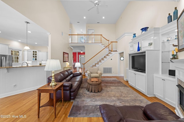 living area featuring a fireplace, a ceiling fan, visible vents, stairway, and light wood finished floors