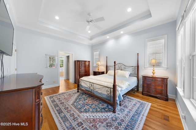 bedroom featuring a tray ceiling, light wood-style flooring, ornamental molding, visible vents, and baseboards
