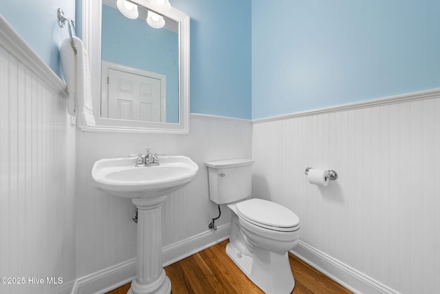 bathroom with toilet, wood finished floors, and a wainscoted wall