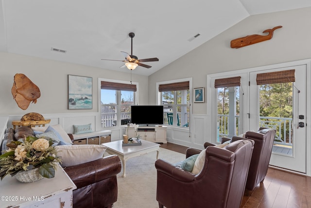 living area featuring visible vents, a wainscoted wall, vaulted ceiling, and wood finished floors