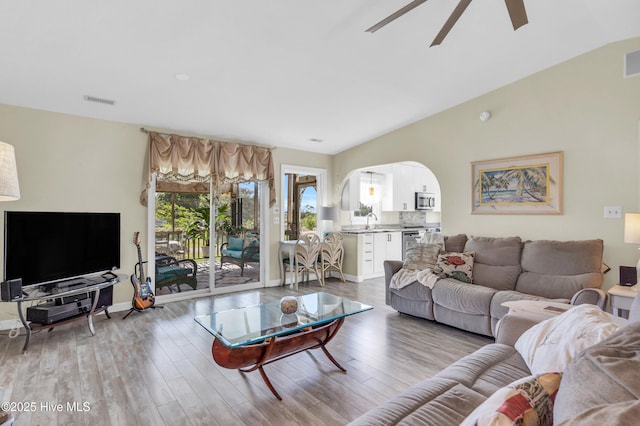 living area with arched walkways, a ceiling fan, visible vents, and light wood finished floors