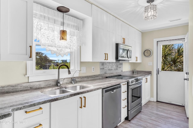 kitchen with light wood-type flooring, white cabinets, a sink, appliances with stainless steel finishes, and decorative light fixtures