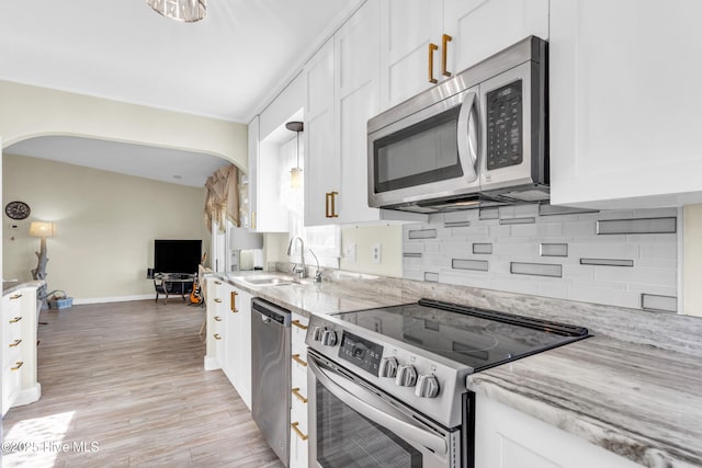 kitchen featuring backsplash, light stone countertops, a sink, stainless steel appliances, and white cabinetry