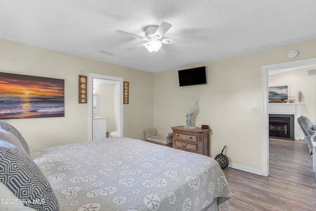 bedroom featuring visible vents, wood finished floors, a fireplace, baseboards, and ceiling fan