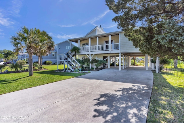coastal inspired home with a front lawn, covered porch, driveway, stairway, and a carport
