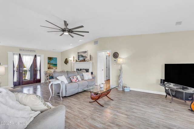 living area with visible vents, wood finished floors, baseboards, ceiling fan, and vaulted ceiling