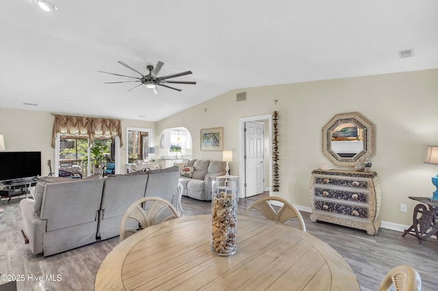 dining space with ceiling fan, arched walkways, vaulted ceiling, wood finished floors, and baseboards