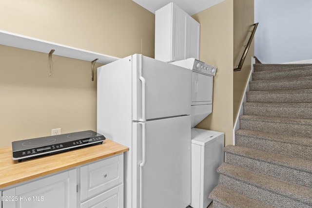 interior space with wood counters, stacked washer and dryer, white cabinetry, and freestanding refrigerator