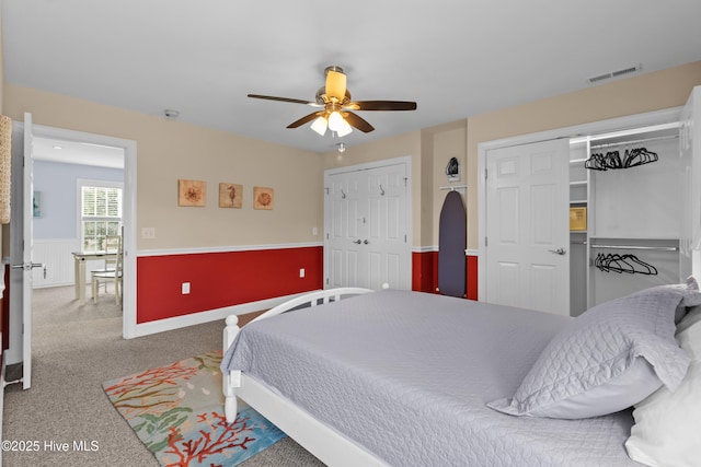 bedroom with two closets, ceiling fan, visible vents, wainscoting, and carpet floors