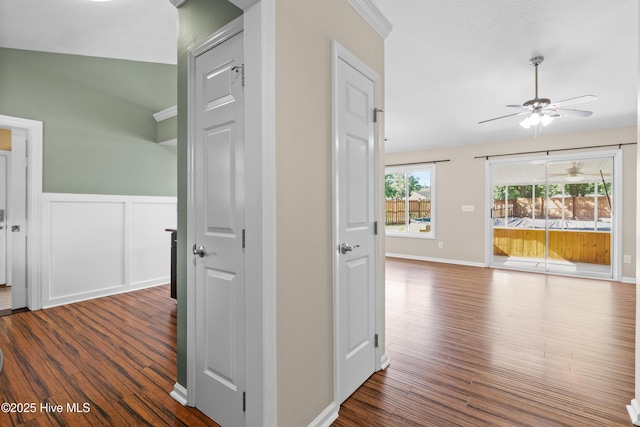 hall with dark wood-style floors, a wainscoted wall, and baseboards