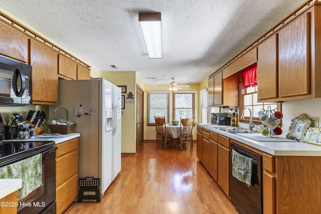 kitchen featuring a sink, a textured ceiling, light wood-type flooring, light countertops, and black appliances