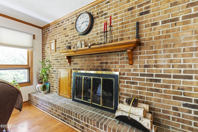 interior space featuring a brick fireplace, wood finished floors, crown molding, baseboards, and a textured ceiling