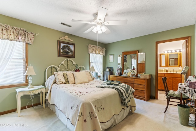 bedroom with a sink, ensuite bathroom, ceiling fan, light colored carpet, and visible vents