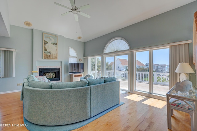 living area featuring light wood-style floors, a fireplace, ceiling fan, high vaulted ceiling, and baseboards