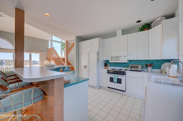 kitchen with tasteful backsplash, a breakfast bar area, white appliances, and a sink