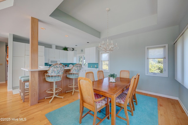 dining space featuring light wood-style flooring, a raised ceiling, a chandelier, baseboards, and recessed lighting