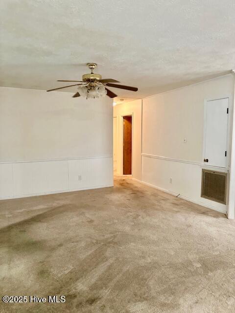 spare room featuring a textured ceiling, a ceiling fan, visible vents, and wainscoting