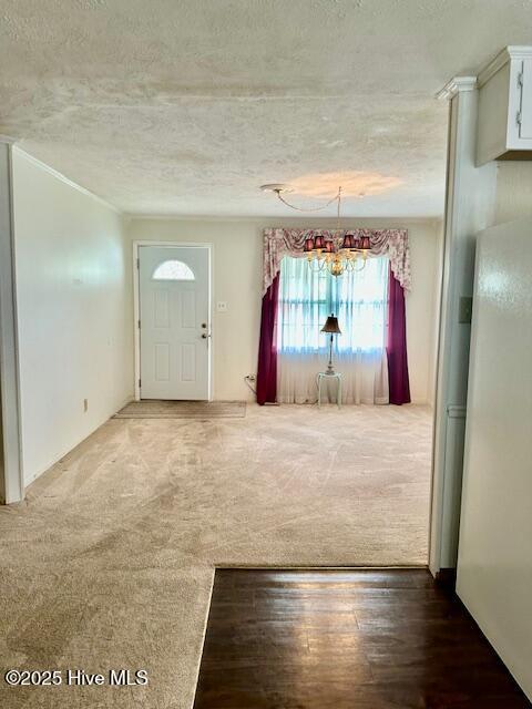 carpeted entrance foyer featuring an inviting chandelier, wood finished floors, and a textured ceiling
