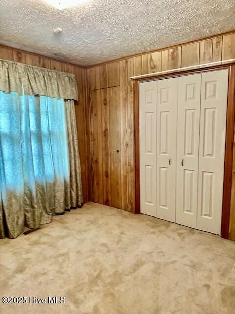 unfurnished bedroom featuring a textured ceiling, a closet, wood walls, and carpet flooring