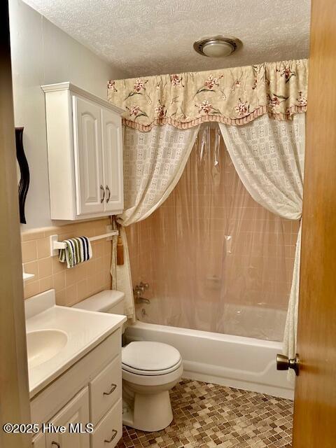 bathroom featuring vanity, a textured ceiling, toilet, shower / bathtub combination with curtain, and tile walls