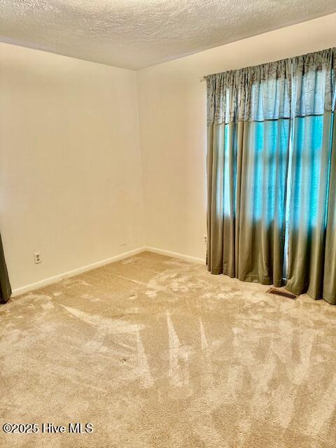 carpeted spare room featuring a textured ceiling and baseboards