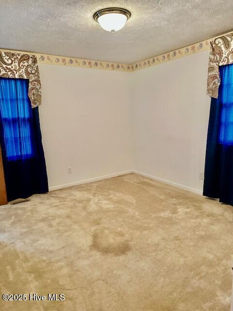 carpeted empty room featuring a textured ceiling and baseboards