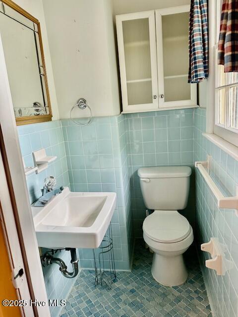 bathroom featuring a sink, tile walls, toilet, and a wainscoted wall