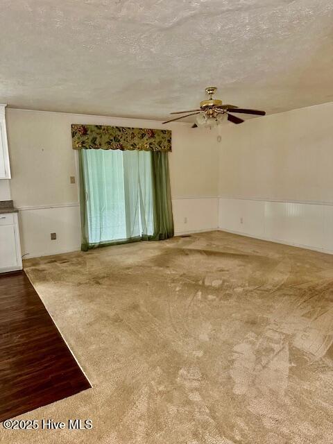 unfurnished room with carpet floors, ceiling fan, wainscoting, and a textured ceiling