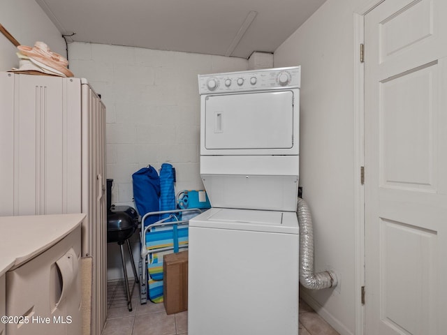 clothes washing area featuring stacked washing maching and dryer, light tile patterned flooring, concrete block wall, and laundry area