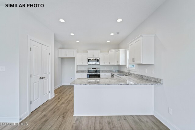 608 Indigo Johnston Dr, Jacksonville, NC 28546 - kitchen with a peninsula, white cabinets, light stone countertops, appliances with stainless steel finishes, and a sink