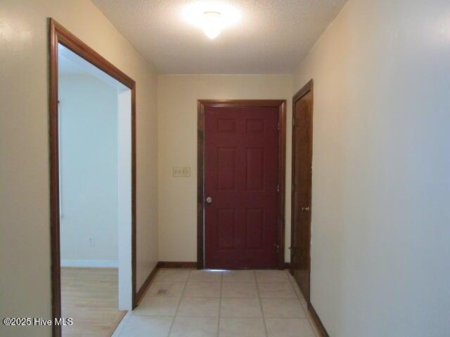 hall featuring baseboards, light tile patterned flooring, and a textured ceiling