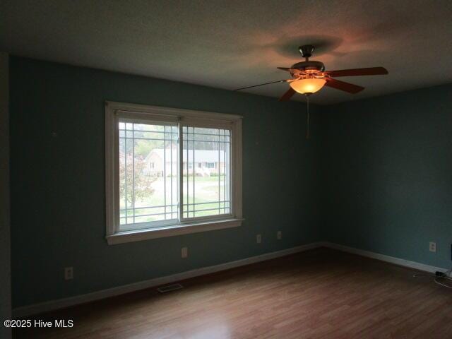empty room with wood finished floors, ceiling fan, baseboards, and visible vents